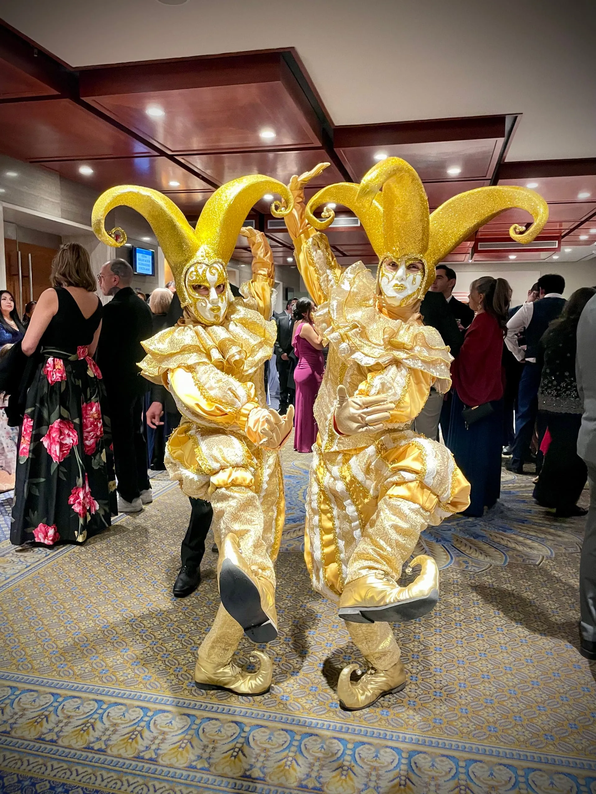 Arlequines con trajes y sombreros dorados recibiendo a los invitados